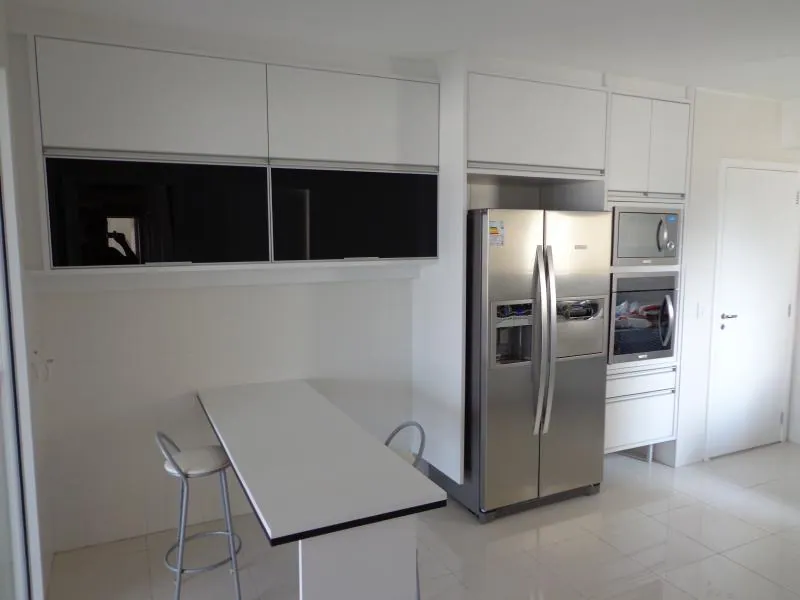 Cozinha planejada branca com mesa de apoio e torre de fornos