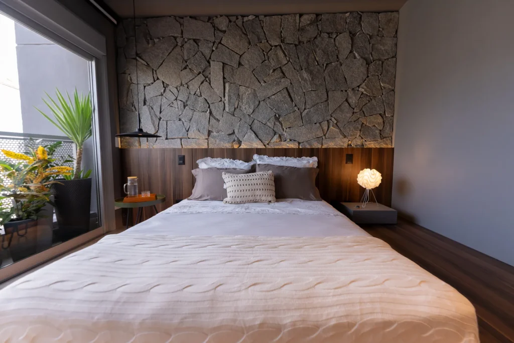 Quarto com cama plataforma em madeira e parede de pedra em Pinheiros